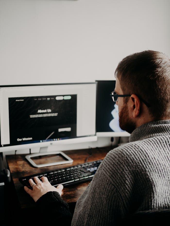 about-01 Man working on web design at home office setup with dual monitors.